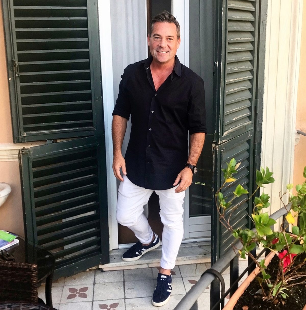 Tony Parmelee, smiling, standing in a doorway between green shutters
